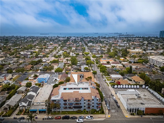 Aerial panoramic view of a residential area with a blend of houses and multi-story buildings, extending towards the ocean in the background.