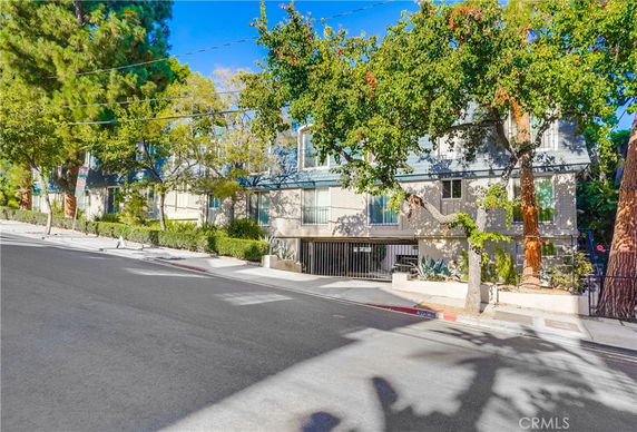 Front view of a multi-story residential building with trees along the sidewalk.