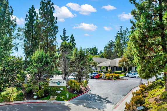View of a building surrounded by trees with a parking area in front.