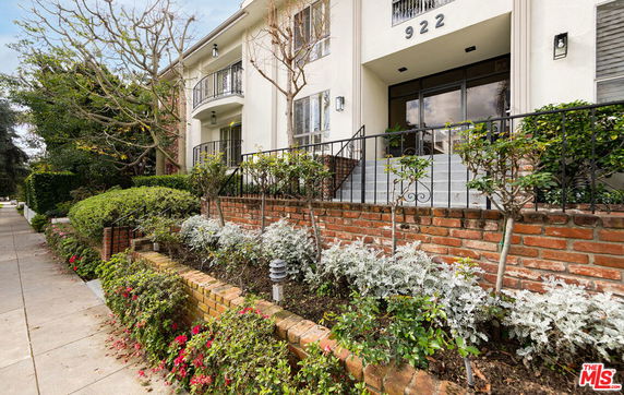 Front view of a multi-story building with a brick and stucco facade, featuring a staircase and landscaped front area.