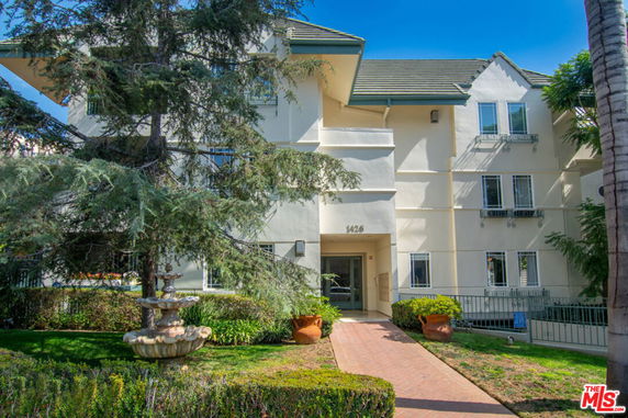 Front view of a multi-story residential building with a pathway and fountain in the foreground.