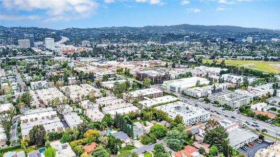 Aerial panoramic view of a city with buildings, roads, and hills in the background.