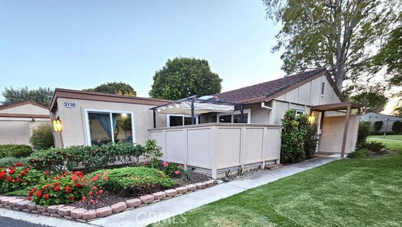 Front view of a single-story house with a pergola-covered patio and garden.