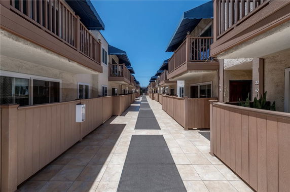 View of a pathway between two rows of townhouses with upper balconies and fenced lower patios.