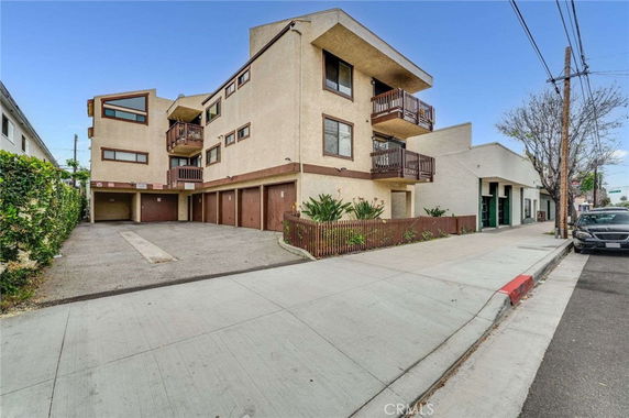 Front view of a multi-story apartment building with balconies and a parking area.