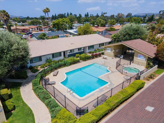Aerial view of a swimming pool and hot tub with a surrounding fence next to a single-story building.