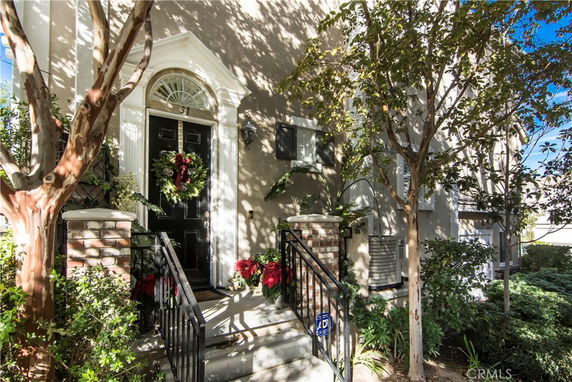 Front view of a house with a decorated entryway, featuring a black door, brick pillars, and surrounding trees.