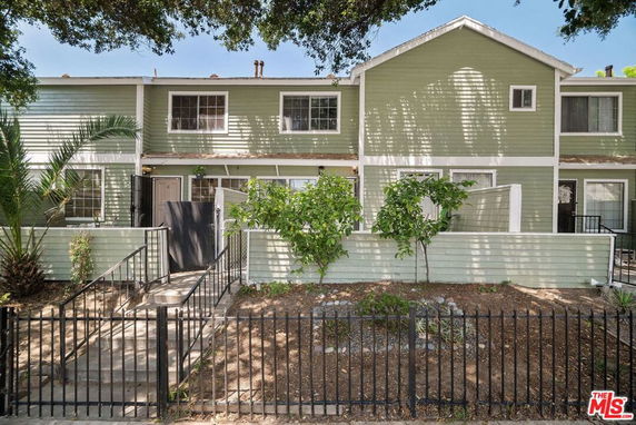 Front view of a two-story residential building with green siding and a fenced entrance.