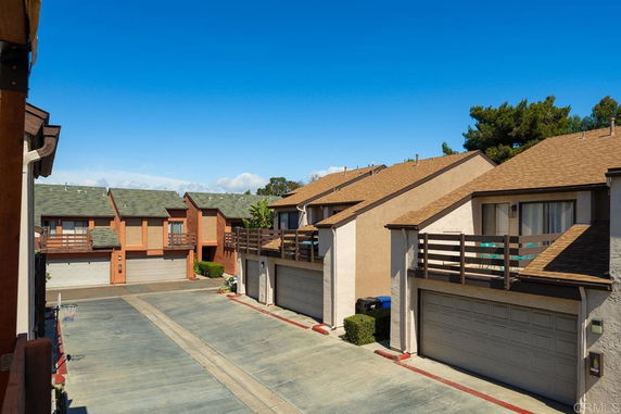 Residential townhouses with garages and balconies, viewed from a driveway.