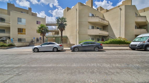 Front view of a multi-story building with balconies and parked cars.