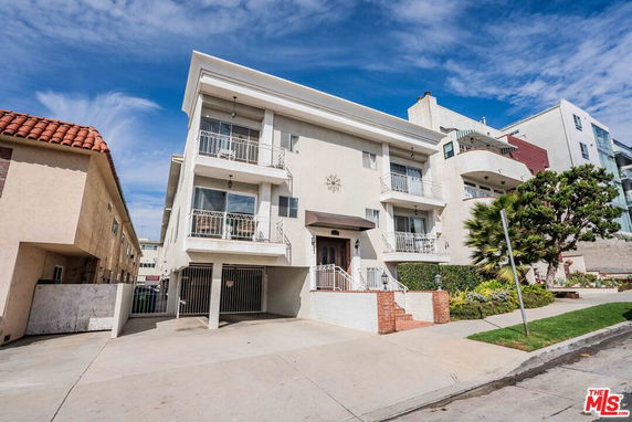 Front view of a three-story residential building with balconies and a gated entrance.