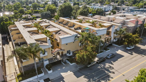 Front view of a multi-story building with balconies and palm trees along the street.
