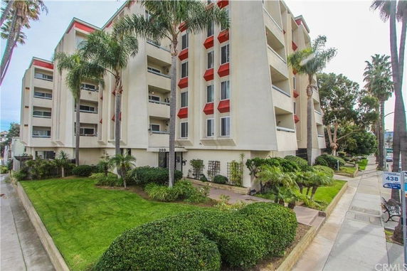 Front view of a multi-story apartment building with balconies and palm trees.