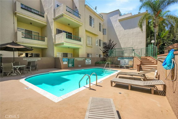 Outdoor swimming pool area adjacent to a multi-story building with balconies.