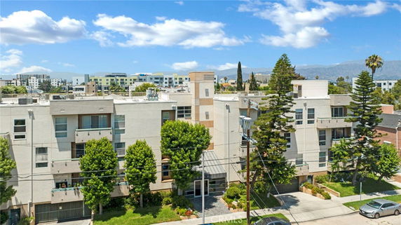 Front view of a multi-story residential building with a flat roof and balconies, surrounded by trees.