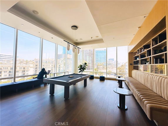 Interior view of a room with a pool table and seating area, featuring large windows and shelves.