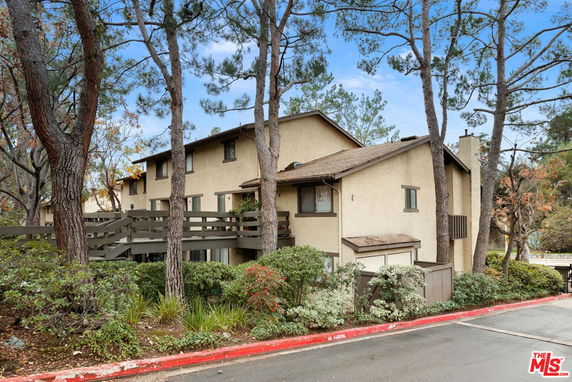 Front view of a multi-story house with a wooden balcony and surrounded by trees.