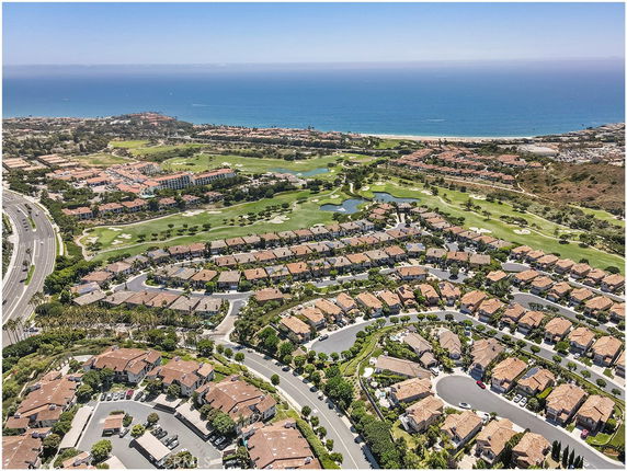 Aerial view of a residential neighborhood with winding streets and red-roofed houses near the coast.
