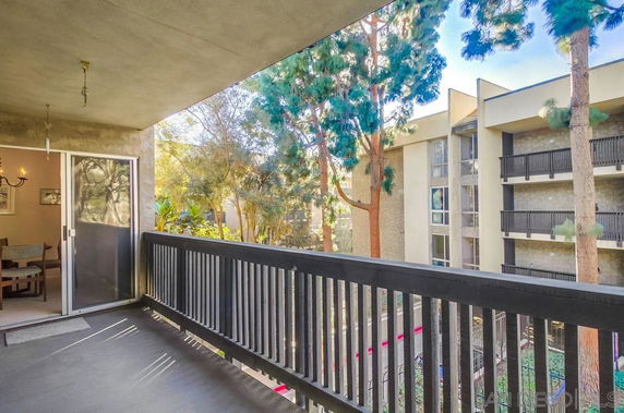 Balcony view from a residential building overlooking another apartment complex and trees.