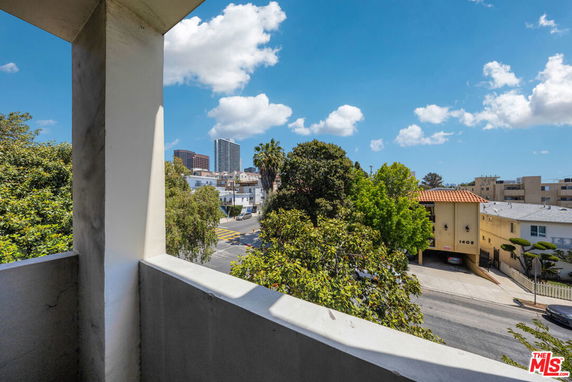 View of surrounding area from a balcony with buildings and trees visible.