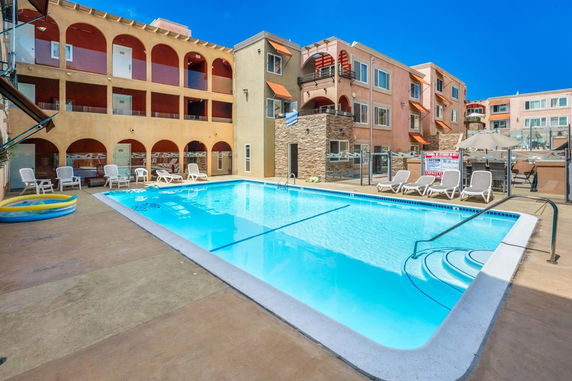Outdoor swimming pool area with lounge chairs and multi-story building in the background.