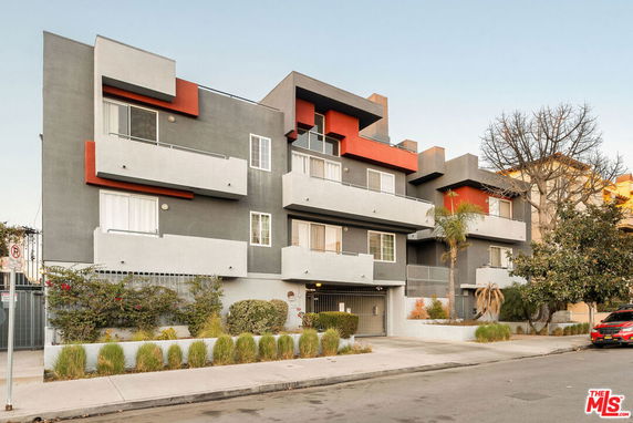 Front view of a modern multi-story apartment building with balconies and a mix of gray and red exterior colors.