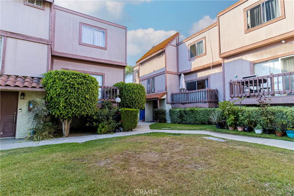 Front view of a multi-story residential building with balconies and a small garden area.