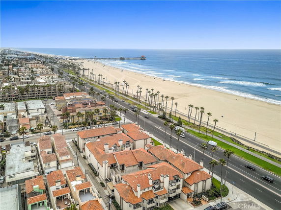 Aerial view of beachfront buildings with red roofs and a nearby road, overlooking a sandy beach and ocean.
