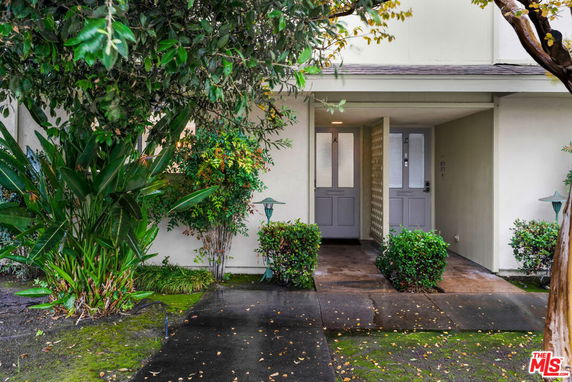 Front view of a house entrance with a covered walkway and surrounding greenery.