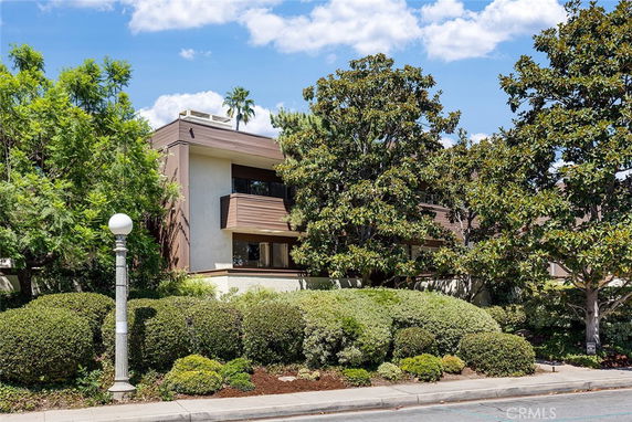 Front view of a multi-story building with balconies and surrounded by trees.
