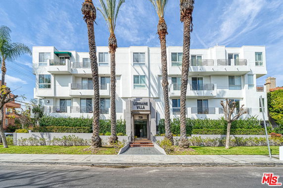 Front view of a multi-story apartment building with balconies and palm trees in front.