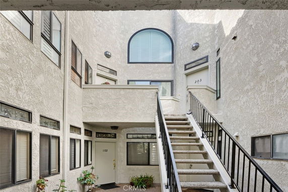 Entrance view of a stucco apartment building with stairs leading to upper floors.