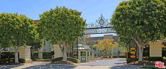 Front view of a gated entrance with decorative ironwork and a small guardhouse.