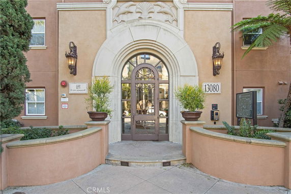 Front entrance of a beige building with an arched doorway and decorative lighting.