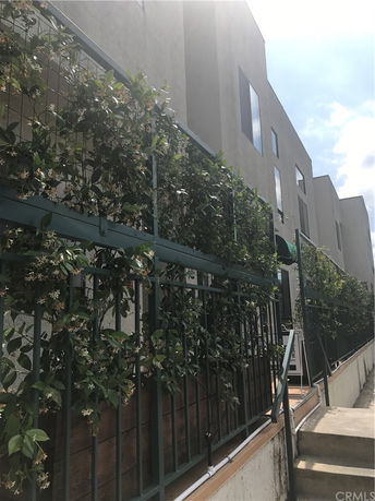 Front view of a multi-story building with a fence covered in greenery.