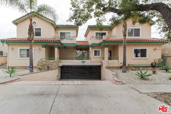Front view of a two-story duplex with a central gated entrance and surrounding palm trees.