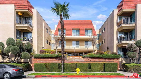Front view of a multi-story apartment building with balconies and a red-tiled roof.