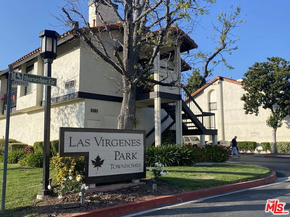 Front view of a townhome building with exterior stairs and a sign reading 'Las Virgenes Park Townhomes'.