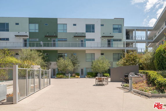Front view of a modern multi-story building with balconies and a landscaped area.