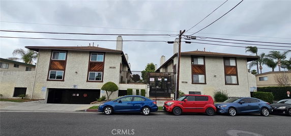 Front view of a multi-story residential building with parked cars and a gated entrance.