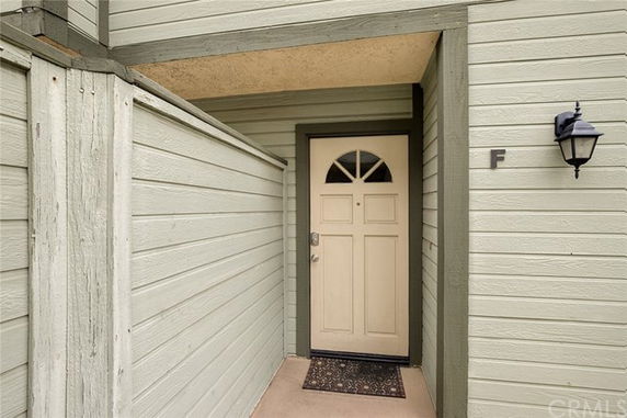 Entryway of a building with a beige door marked with letter F and a wall-mounted light fixture.