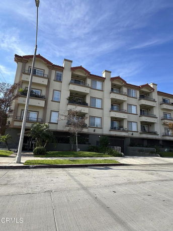 Front view of a multi-story apartment building with balconies and a red-tiled roof.