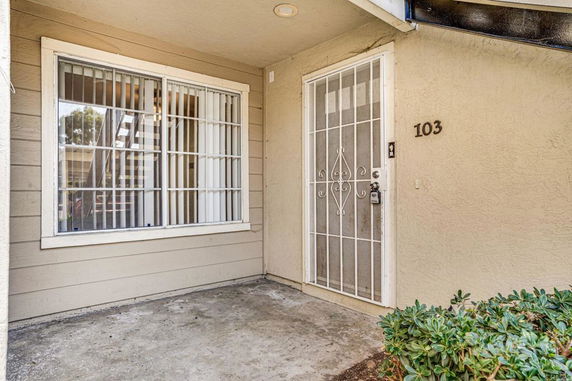Front view of a house entrance with a metal security door and windows with vertical blinds.