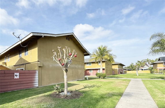 Front view of a two-story building with a sloped roof and windows, featuring a side patio area.