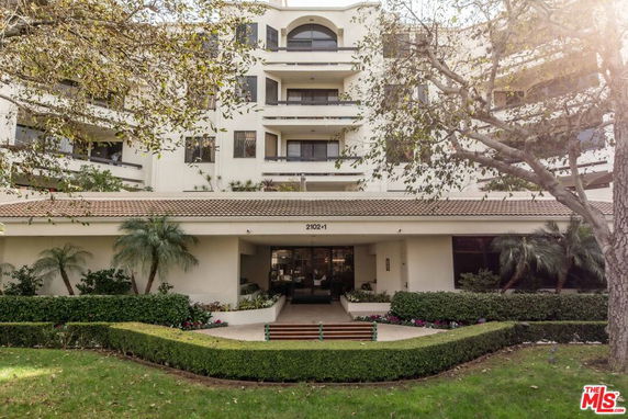 Front view of a multi-story residential building with balconies and a landscaped entrance.