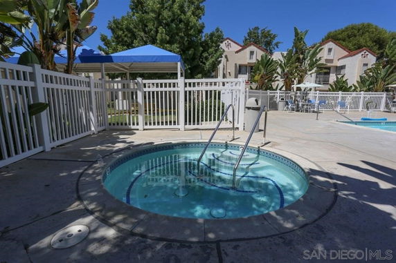 Outdoor area featuring a small round hot tub next to a larger swimming pool, surrounded by a white fence and a gazebo.