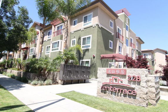 Front view of a multi-story residential building with balconies and a sign in front.