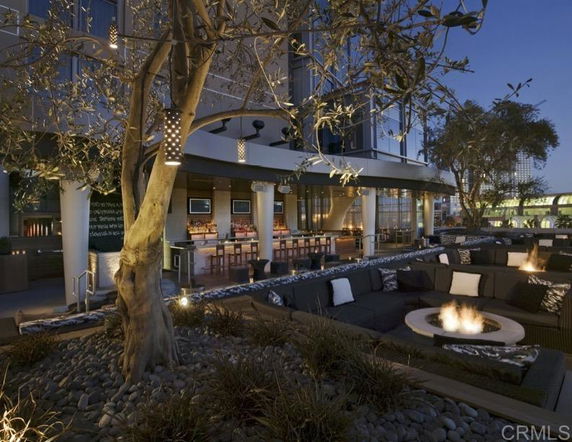 Outdoor seating area with fire pits and a view of a bar and surrounding buildings.