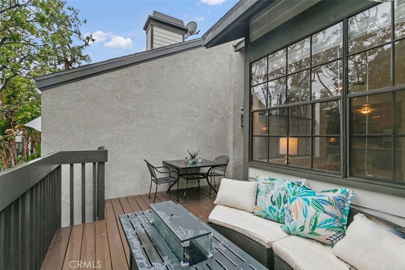 Outdoor seating area on a rooftop deck with a view of large windows and surrounding greenery.