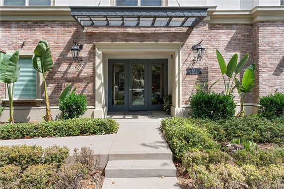 Front view of a brick building entrance with double glass doors and decorative plants.